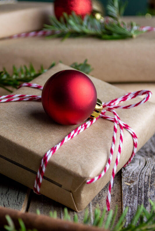 Vánoční dárky zabalené v přírodním papíře, s bílo-červenou šňůrkou a vánoční koulí