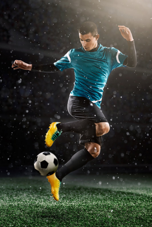 fotbalista na hřišti s míčem, modro-černý dres a žluté kopačky