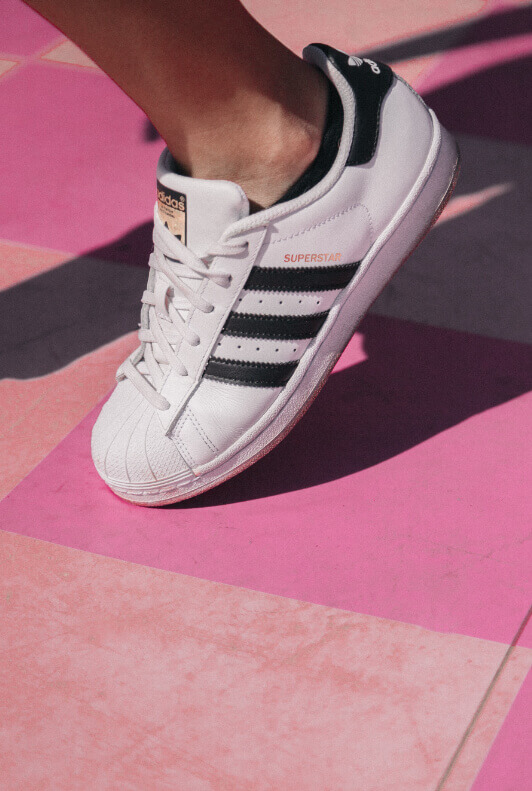 Bílé tenisky Adidas Superstar na růžovém pozadí